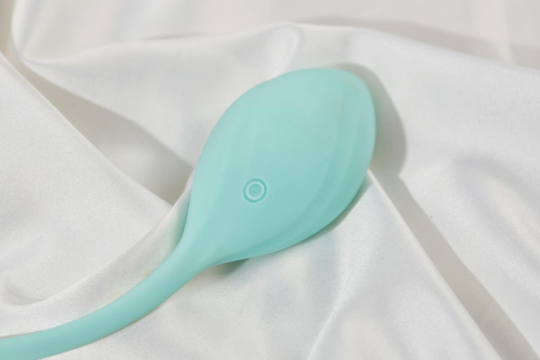A sleek teal clitoral vibrator resting on white silk, demonstrating modern suction toy design