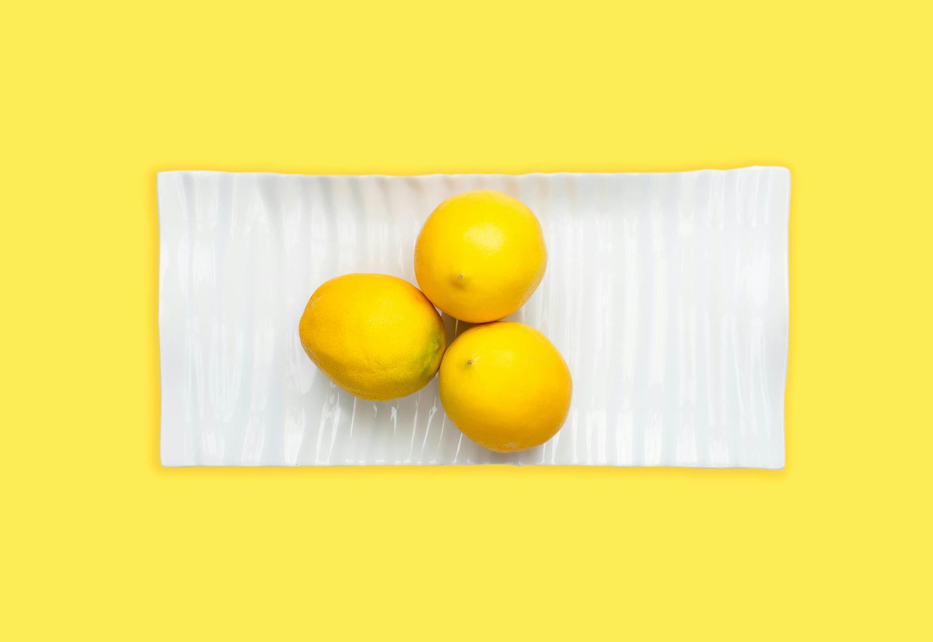 Hand holding a lemon on soft pink background with additional lemons nearby, symbolizing touch sensitivity and citrus freshness