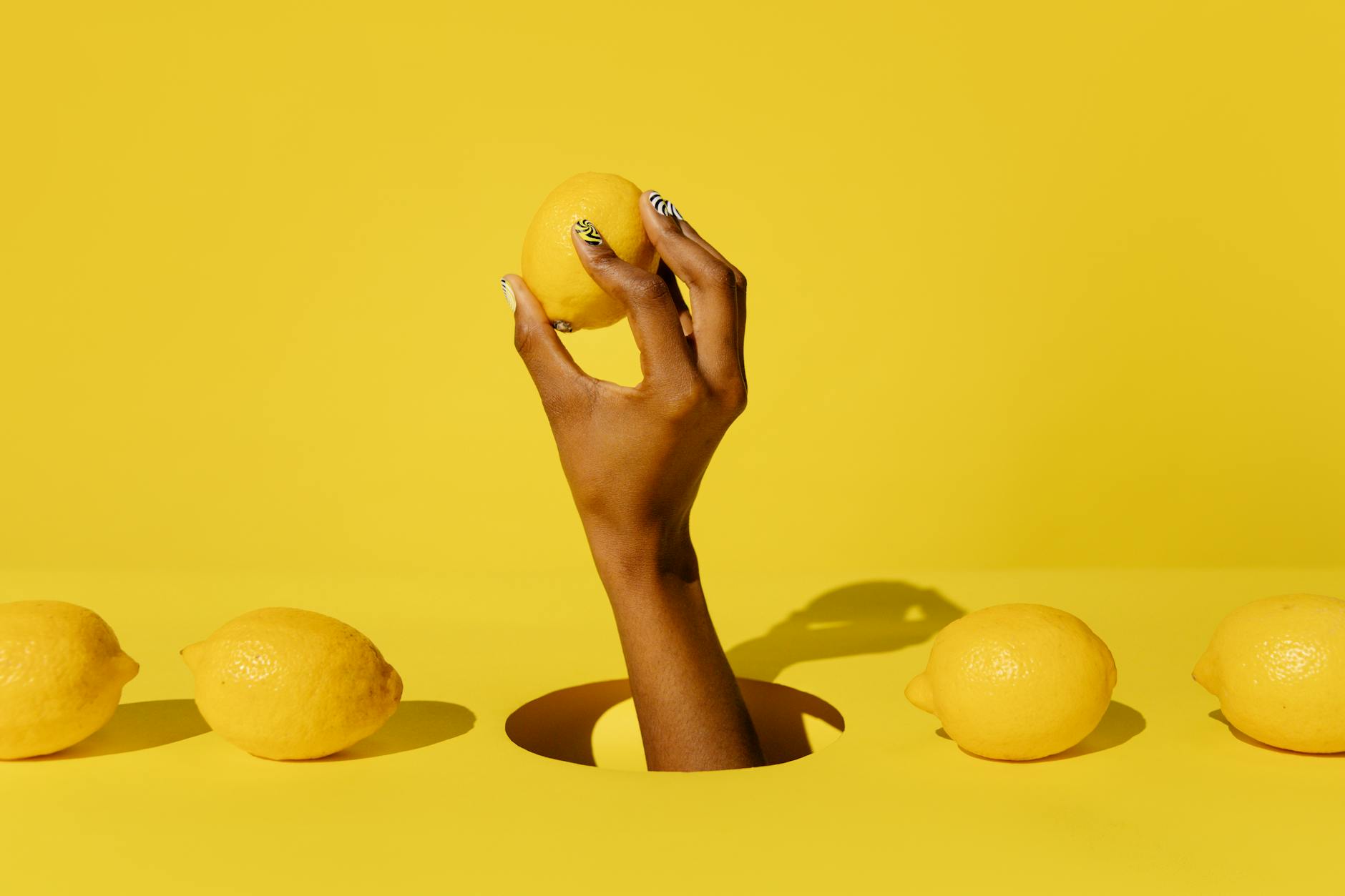 Hand holding a fresh lemon against a bright yellow background, symbolizing the citrus-inspired design of modern clitoral vibrators