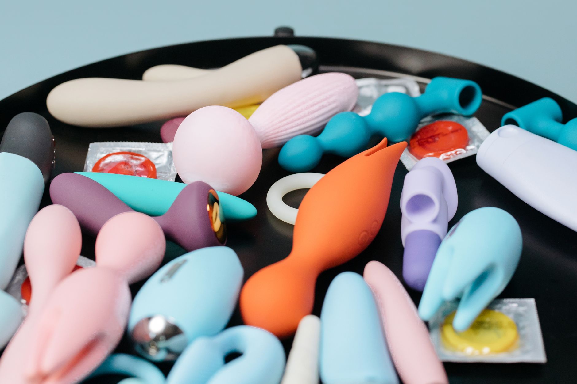 A collection of colorful clitoral vibrators arranged on a black surface, showcasing diverse styles and textures