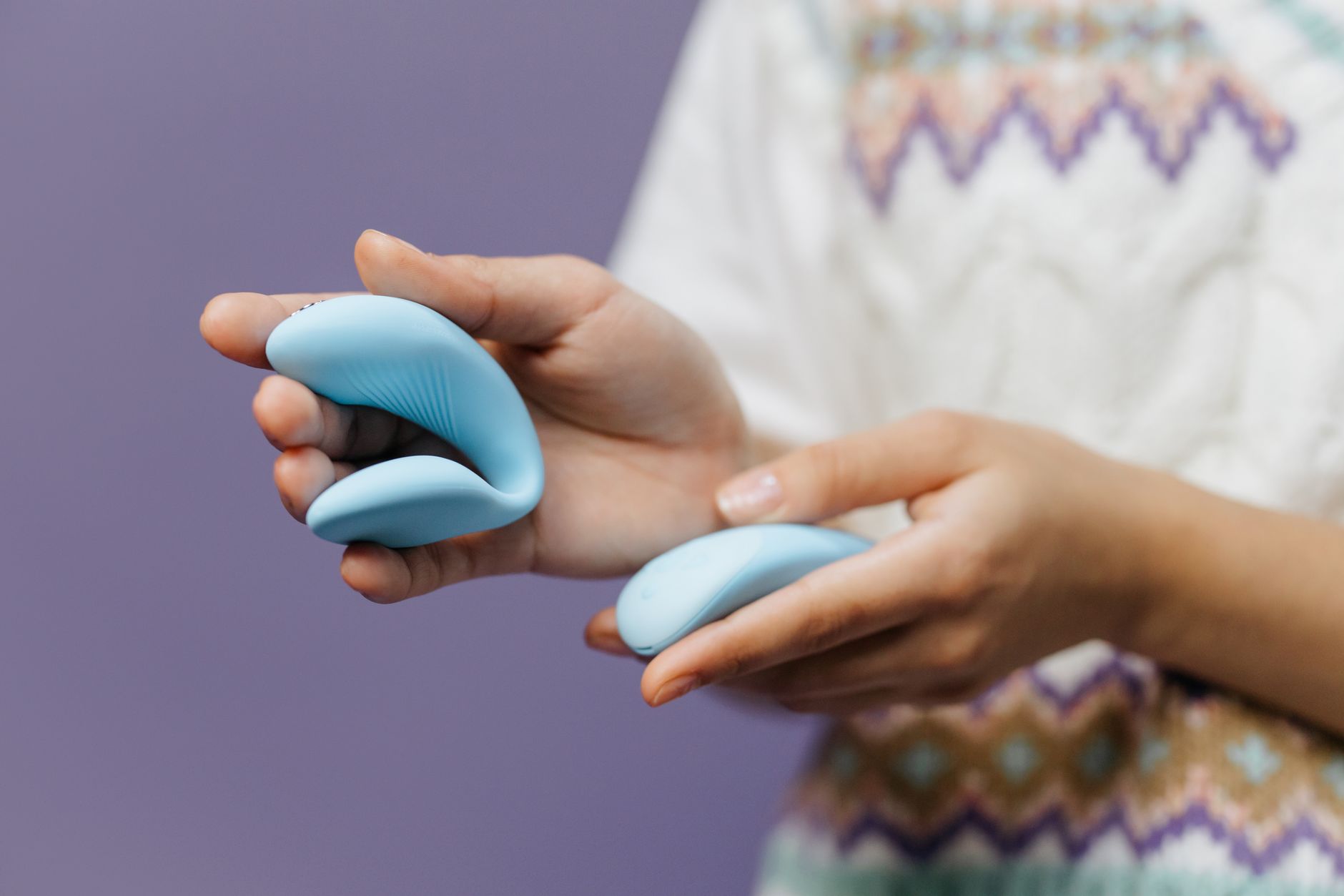 Hands holding a sleek blue vibrator against a soft background