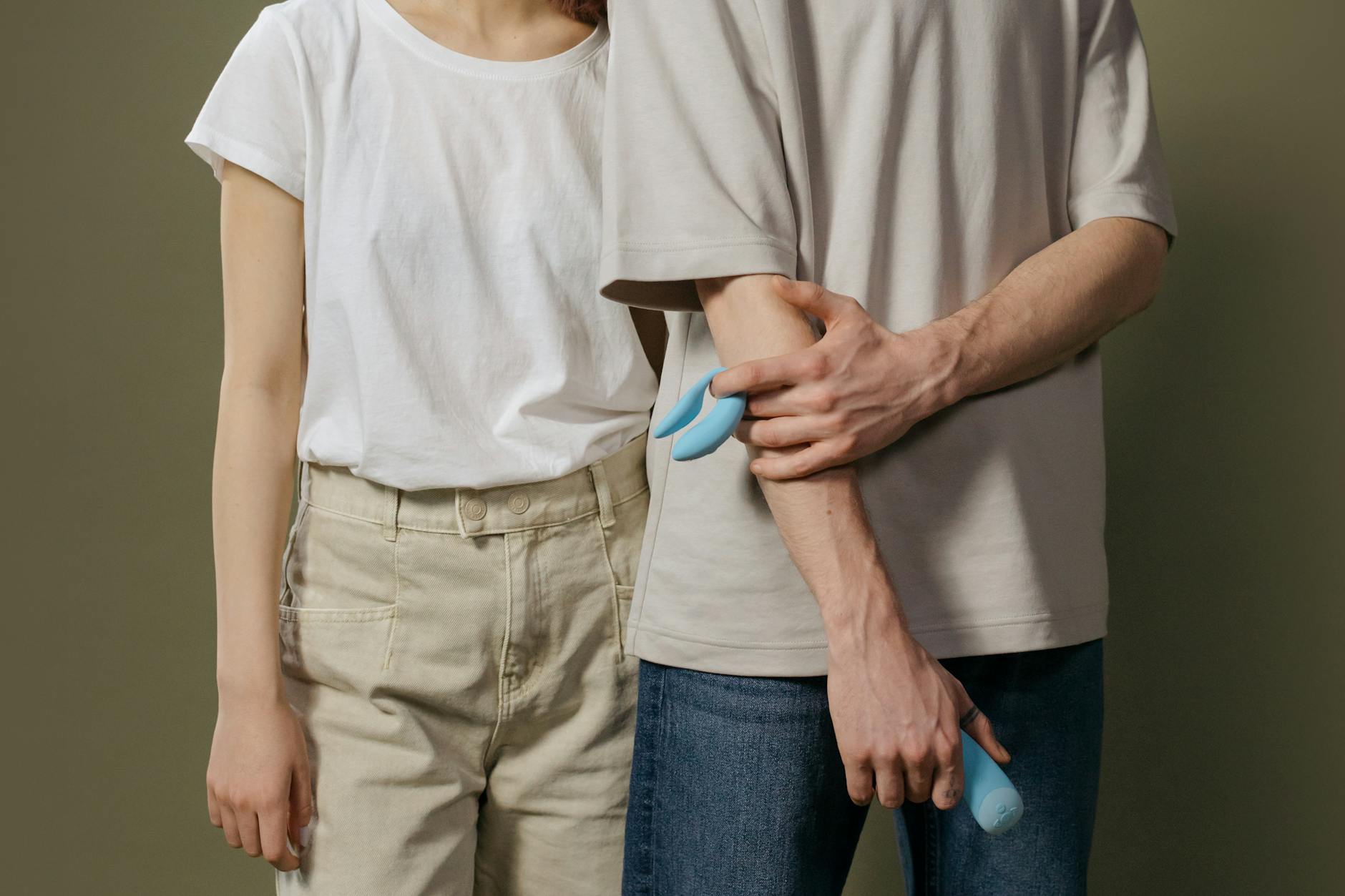 A young couple standing together indoors, holding a blue vibrator, symbolizing modern intimacy.
